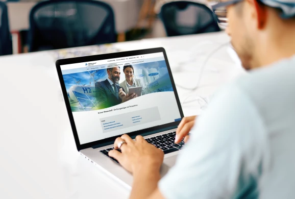Mann tippt auf einem Laptop, auf dem die Website von TÜV Rheinland zu sehen ist