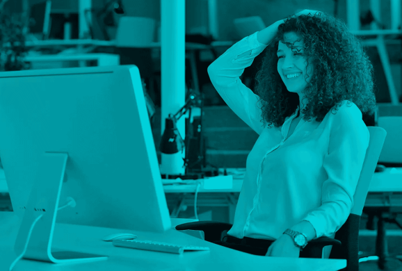 Frau im Büro, die lächelnd vor einem Computer sitzt – Symbolbild für erfolgreiches Prompting in der KI-gestützten Content-Erstellung.