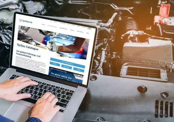 Eine Serviceperson steht mit einem Laptop neben einem geöffneten Motorraum und betrachtet die TecAlliance Website