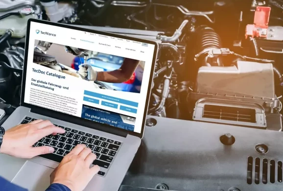 Eine Serviceperson steht mit einem Laptop neben einem geöffneten Motorraum und betrachtet die TecAlliance Website
